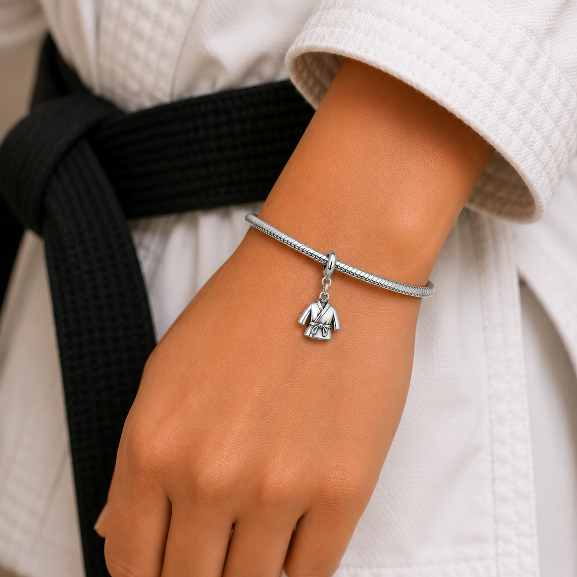 Close-up of a person wearing a silver bracelet with a pendant, dressed in a white martial arts uniform with a black belt.