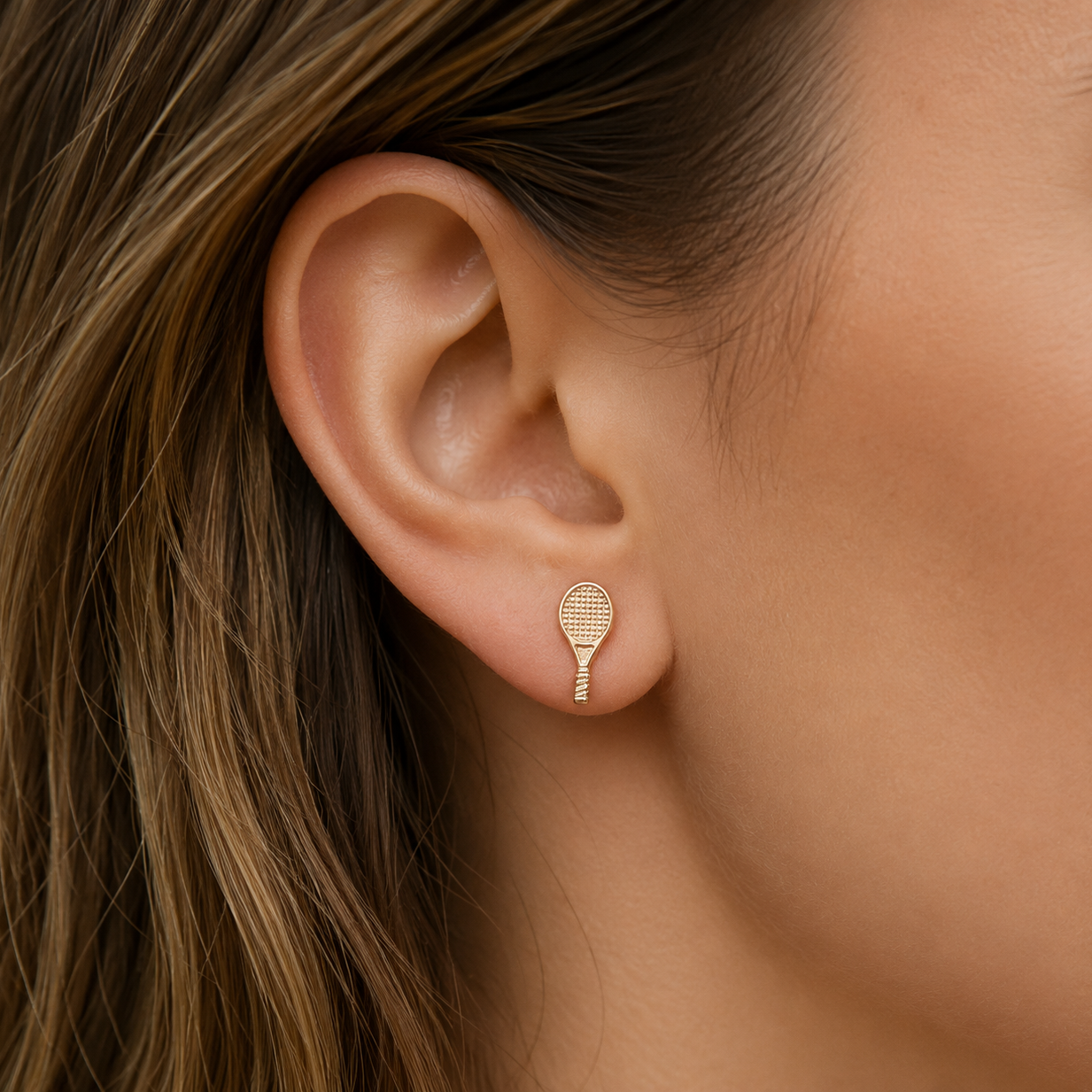 Gold earring worn by a person with brown hair.