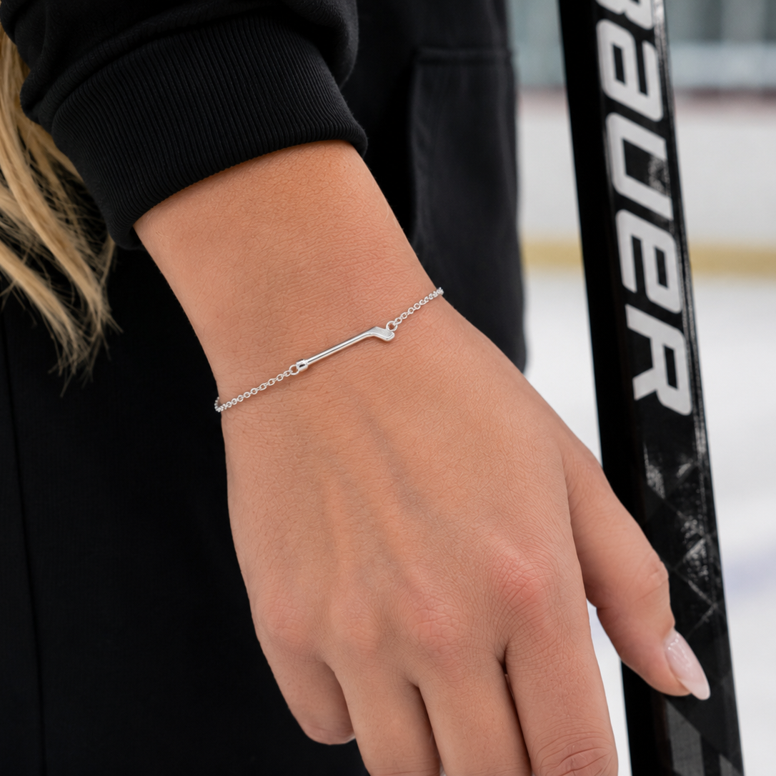 Hand wearing a silver bracelet with a blurred hockey stick in the background